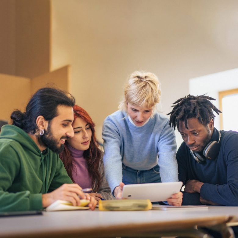 Digital learning concept, diverse university students collaborating around a tablet in a bright classroom.